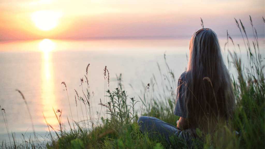 Woman meditating at sunrise by the water to calm anxiety naturally